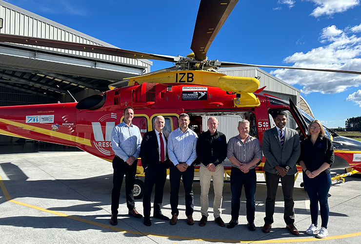 Seven people standing in front of a red and yellow helicopter